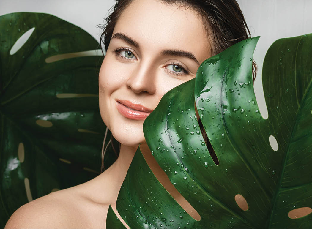 Portrait of beautiful young woman with a smooth skin holding Monstera deliciosa plant leaf