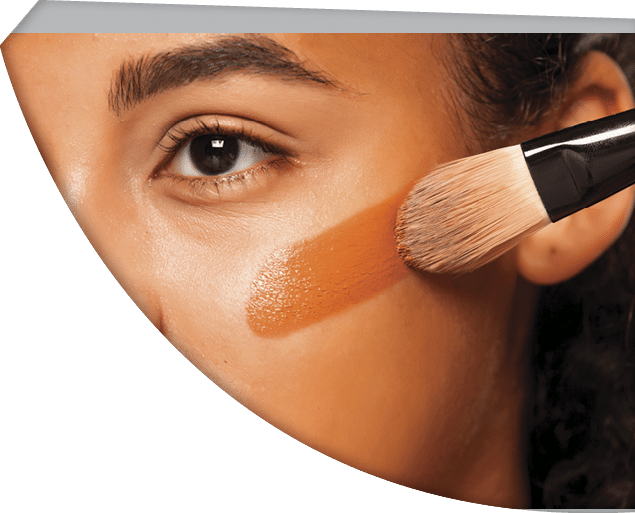 portrait of a young dark-skinned woman applying liquid makeup base with brush on her face on a white background