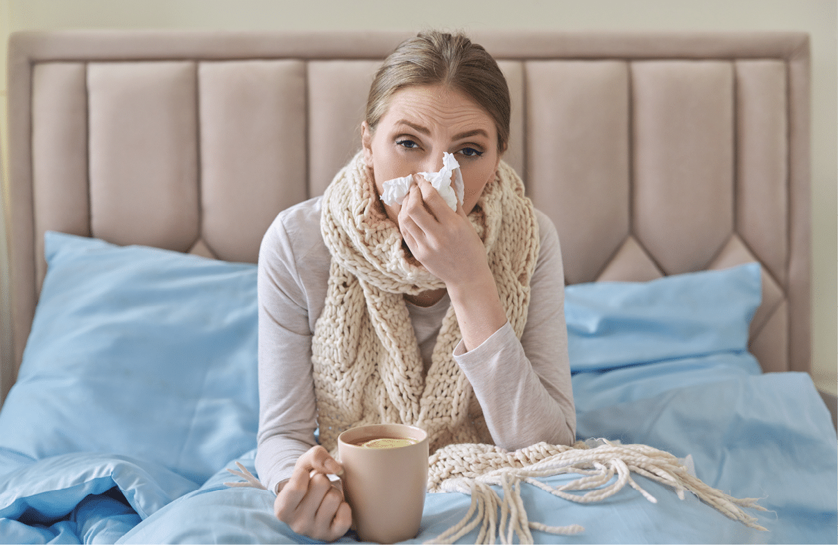 Sick young woman sitting at home in bed with hot cup of tea and handkerchief  Seasonal colds, cough, runny nose, viral infections, home treatment