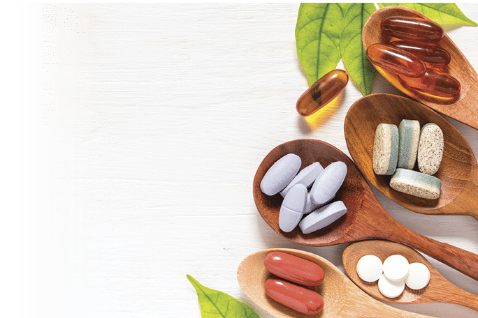Variety of vitamin pills in wooden spoon on white background with green leaf, supplemental and healthcare product, flat lay surface