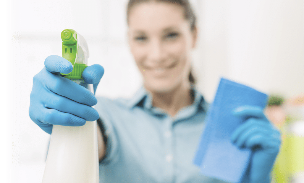 Smiling young housewife doing chores and spraying a cleaning product, hand and bottle close up, selective focus