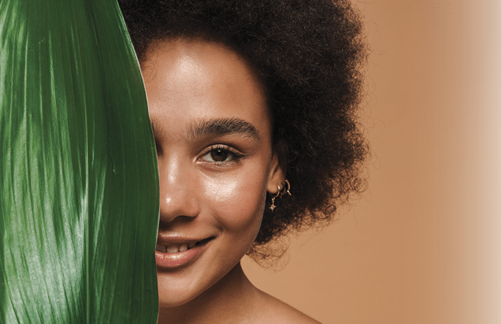 Black shirtless woman smiling while posing with green leaf isolated over beige background