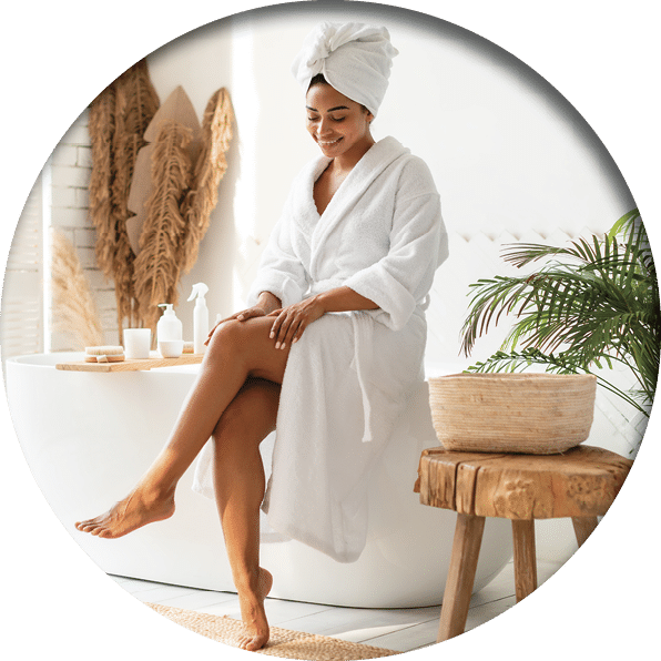 Pretty African American Female Touching Smooth Legs After Depilation Posing Sitting On Bathtub In Bathroom Indoor. Full Length Shot Of Lady Enjoying Beauty Routine And Caring For Body