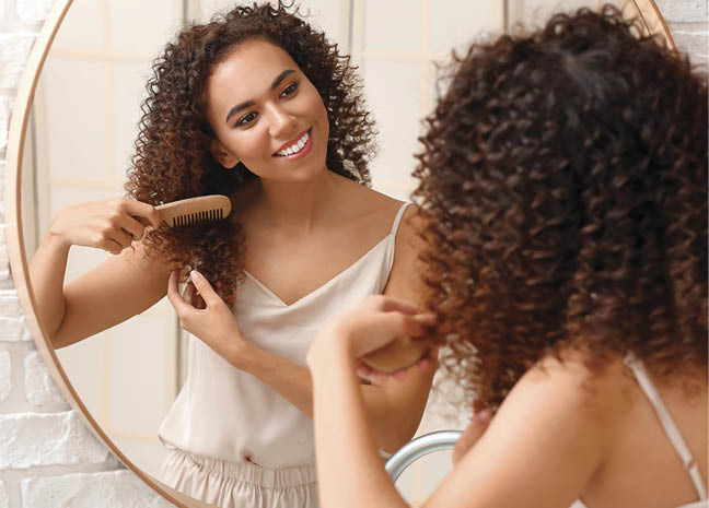 Young African-American woman combing her hair near mirror in bathroom