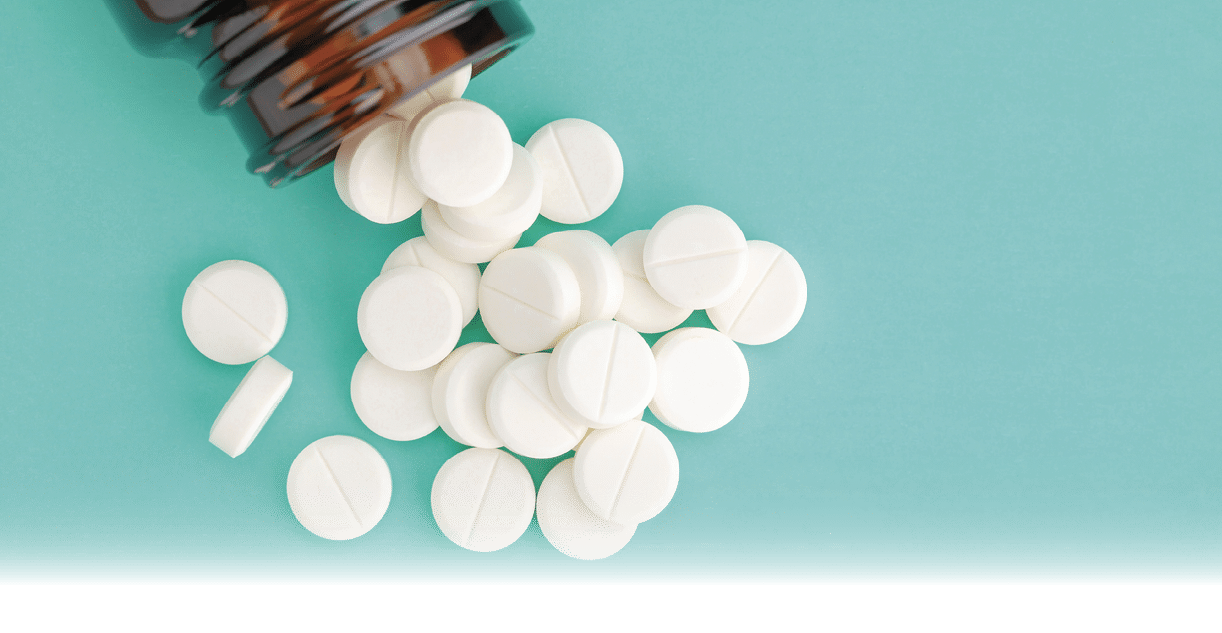 White round tablets scattered in front of glass bottle of pills