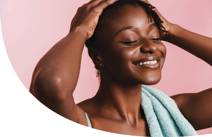 Black shirtless woman with towel smiling and looking at camera isolated over pink background