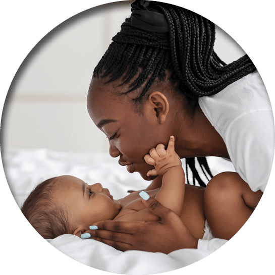 Black mom playing in bed with her infant, kissing baby