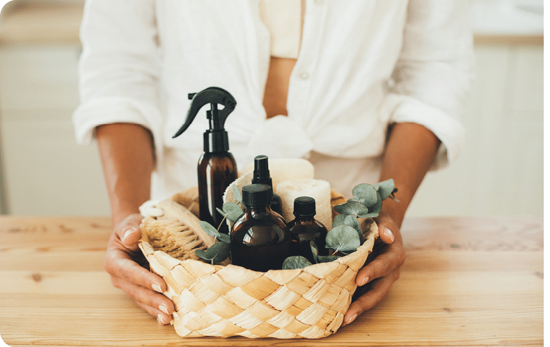 Woman holding wicker basket with natural eco-friendly zero waste plastic free cleaning items: brushes, rugs, soap, essential oils, spray and sponges at the kitchen. Plastic free home.