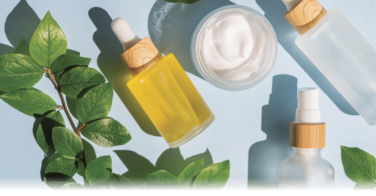 Blank frosted glass spray bottle and bamboo jar on blue background with green leaves. Organic spa cosmetic beauty product mock up