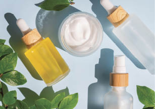 Blank frosted glass spray bottle and bamboo jar on blue background with green leaves. Organic spa cosmetic beauty product mock up