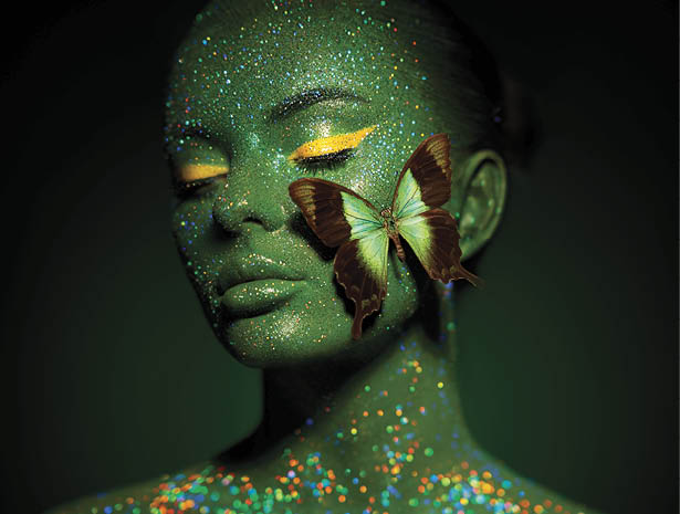 Fashion model woman skin face in bright sparkles with green butterfly colorful neon lights, beautiful girl sexy lips. Glowing art green skin make-up. Glitter metallic shine silver green makeup