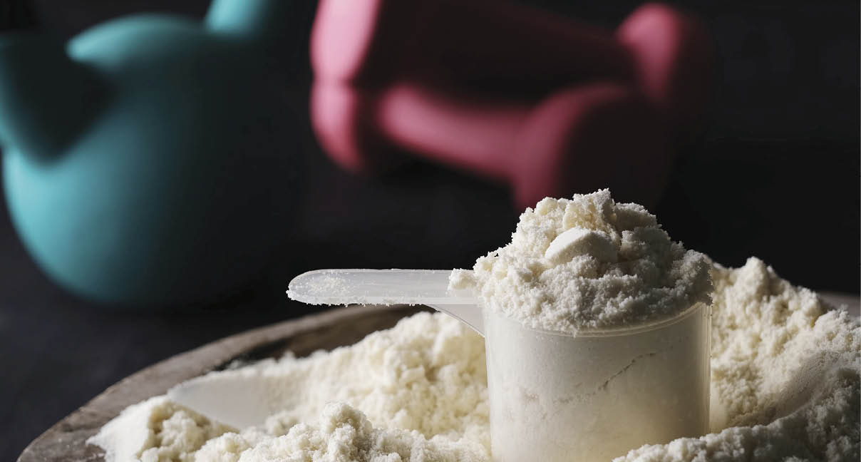Measuring spoon with dry sports protein with sport equipment on a table